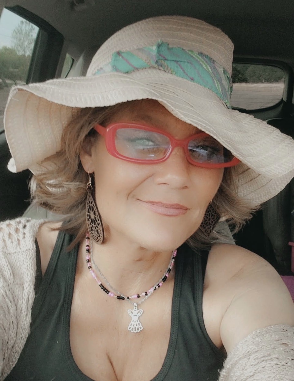 Portrait of Pam H. Frank, founder and elite mobile massage therapist behind The Traveling Tea Party, smiling in a wide-brim hat and red glasses.